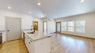 Located at 102 E Farwell in Spokane, WA, this thoughtfully designed 2-bedroom, 1-bathroom unit offers a clean, modern aesthetic throughout its well-utilized single-floor layout. The open-concept kitchen and living area serves as the heart of the home, anchored by a large center island with a quartz countertop, undermount sink, and matte black fixtures. White shaker cabinetry pairs seamlessly with stainless steel appliances, including a French door refrigerator, range, and microwave. Light wood-tone flooring runs continuously throughout the space, enhancing the bright, airy atmosphere created by recessed lighting and abundant natural light. The living area opens to a private balcony through a glass-panel door, flanked by a bank of windows framing lush wooded views. A wall-mounted mini-split system provides efficient climate control in both the living area and bedrooms. The primary bedroom is a comfortable, sunlit retreat with a double-pane window overlooking the trees and its own mini-split unit. The second bedroom offers similar natural light and a stylish ceiling fixture. The bathroom features a wide gray shaker vanity, round mirror with contemporary lighting, and matching wood-tone flooring, rounding out this clean and functional living space.