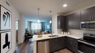 Located at 3400 E Southern Ave in Phoenix, AZ, this single-story residence offers a thoughtfully designed open-concept layout with modern finishes and a cohesive contemporary aesthetic. The kitchen is a standout feature, equipped with dark espresso cabinetry, crisp white quartz countertops, stainless steel appliances — including a range, microwave, dishwasher, and refrigerator — and a peninsula with bar seating. Cylindrical pendant lights provide focused illumination, while wood-style flooring flows seamlessly into the connected dining and living areas. The living room is bright and welcoming, anchored by a soothing blue accent wall, large windows with horizontal blinds that invite natural light, and a ceiling fan overhead. The bedrooms are carpeted for comfort, each offering ample natural light through generously sized windows with linen drapery and ceiling fans. The bathroom features dark cabinetry consistent with the kitchen design, a wide vanity with white countertop, a tub-shower combination, and wood-style flooring. Throughout the space, the design balances neutral tones with warm wood accents, creating an inviting and functional living environment well-suited to the Phoenix lifestyle.