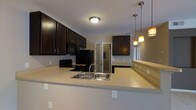 Located at 747 Worthington Woods Blvd in Worthington, Ohio, this single-floor residence offers a thoughtfully designed living space with a cohesive, modern aesthetic. The kitchen is a standout feature, showcasing rich dark espresso cabinetry that contrasts elegantly with light countertops. A spacious peninsula with an extended breakfast bar provides generous prep space and casual seating, making it ideal for both cooking and entertaining. The kitchen is equipped with black appliances, including a range and refrigerator, and features a stainless steel sink. Stylish pendant lighting hangs above the breakfast bar, adding warmth and a refined finishing touch to the space. The layout is open and functional, with a clear sightline connecting the kitchen to the surrounding living areas, creating a sense of flow throughout the home. Neutral wall tones and consistent flooring contribute to a clean, welcoming ambiance. A mirrored accent in the background adds depth to the space, while recessed cabinetry in an adjacent area hints at additional storage and utility. Overall, this residence combines practical design with contemporary finishes for comfortable, everyday living.