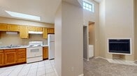 This single-floor residence offers a well-organized layout with a variety of functional living spaces. The living room is a standout area, featuring soaring vaulted ceilings, a ceiling fan, and a tiled fireplace that serves as a focal point — all complemented by plush carpeted flooring that adds warmth to the room. A bright, light-filled nook or dining area features multiple large windows with blinds along two walls, allowing generous natural light to fill the space via light tile flooring.

The kitchen is equipped with warm oak cabinetry, granite-style countertops, a stainless steel double sink, and white appliances including an electric range, refrigerator, and dishwasher. An overhead range hood and upper transom windows provide additional ventilation and light. Adjacent to the kitchen, a dedicated laundry alcove houses a stacked washer and dryer unit for added convenience.

The carpeted bedrooms are comfortable and well-sized, with neutral warm-toned walls. The bathroom features a wooden vanity with a single sink, a light-up mirror, tile flooring, and ample under-sink storage. Throughout the residence, a consistent warm beige color palette creates a cohesive and inviting ambiance, making it a practical and comfortable living space.