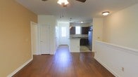 This single-floor residence offers a thoughtfully designed open-concept layout that seamlessly connects the living area, dining space, and kitchen. Rich, dark hardwood flooring extends throughout the main living area, reflecting natural light and adding warmth to the interior. A ceiling fan overhead provides both comfort and a finishing touch to the living space.

The kitchen is a standout feature, showcasing dark espresso cabinetry paired with stainless steel appliances, including a refrigerator and range. A peninsula counter with pendant lighting above serves as both a functional workspace and a casual dining or gathering spot. Light-toned countertops contrast elegantly with the dark cabinetry, and the kitchen transitions into tile flooring for a practical distinction between spaces.

A bright, windowed entryway welcomes residents and guests, allowing natural light to filter into the interior and creating an open, airy feel. Neutral wall tones in warm beige complement both the flooring and cabinetry throughout.

The space also includes interior doors with classic panel detailing and ample wall space, offering versatility for furnishing and personalization. Overall, the residence presents a clean, move-in-ready environment with a cohesive design aesthetic that balances functionality and style.