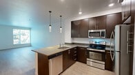 This well-appointed one-bedroom, one-bathroom unit at 28805 Dixon Street, Unit 401 in Hayward, California offers a comfortable and modern living experience across a single floor. The open-concept kitchen and living area serves as the heart of the unit, featuring rich dark-espresso cabinetry, stainless steel appliances including a refrigerator, electric range, and microwave, and a peninsula with a light stone countertop and pendant lighting overhead. Wood-style plank flooring runs throughout, lending a warm, cohesive feel to the entire space. The living area is bright and open, with clean white walls and access to natural light. The spacious bedroom offers a generous footprint, a large window framing views of surrounding greenery, and a sliding closet. A hallway with an electrical panel connects the main living areas to the bedroom and bathroom. The bathroom is well-equipped with a full soaking tub and shower combination, a dark-cabinetry vanity with a light countertop, a wall-mounted medicine cabinet, and wood-style flooring. Clean white walls and recessed and overhead lighting complete the bathroom's functional design. This unit presents a clean, modern aesthetic throughout with consistent finishes that create a cohesive and practical living environment.