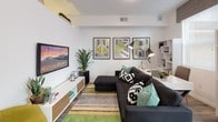 Located at 1125 Avenue of the Oaks in Sparks, Nevada, this single-floor unit offers a thoughtfully designed open layout with modern finishes throughout. The kitchen is a standout feature, showcasing crisp white cabinetry, granite-style countertops, stainless steel appliances including a range and microwave, and a double-basin sink. Open wire shelving adds a contemporary touch, while a compact dining nook with a fold-down table and cushioned chairs makes efficient use of the space. Light wood-look flooring runs seamlessly throughout the unit, creating a warm and cohesive aesthetic. The living area is bright and welcoming, benefiting from large windows that invite abundant natural light. The space is well-suited for both relaxing and working, with room for a sectional sofa, display shelving, and a dedicated workspace. Geometric wall art and teal accent pieces add a modern, curated feel. The bathroom continues the clean, contemporary theme with wood-look tile flooring, crisp white walls, open shelving, and thoughtful decorative touches including framed artwork. The overall ambiance is fresh, light-filled, and modern, making this unit a well-appointed and functional living space in the heart of Sparks, NV.
