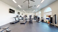 Located at 6710 W Doe Ave in Visalia, California, this fitness center offers a comprehensive, single-floor workout facility designed to support a wide range of exercise routines. The space is defined by its clean, bright aesthetic, with crisp white walls and durable rubber-tile flooring that provides both safety and functionality throughout.

A row of large, arched windows lines one wall, inviting abundant natural light and offering views of the surrounding exterior. Ceiling fans are positioned throughout to maintain comfortable airflow during workouts. Full-length mirrors span one entire wall, visually expanding the space while allowing users to monitor their form.

The cardio zone is well-appointed with multiple treadmills and elliptical trainers, each equipped with individual digital displays. The strength training area includes a multi-station cable machine, a rack of dumbbells ranging across various weights paired with an adjustable bench, and an assortment of functional training accessories including kettlebells and medicine balls. Spin bikes and a rowing machine round out the equipment selection, catering to both high-intensity and low-impact training preferences.

Wall-mounted flat-screen televisions are present throughout the space, adding an entertainment element to cardio sessions. The facility's open layout and generous equipment variety make it a well-rounded destination for fitness enthusiasts of all levels.
