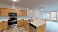 Located in Coeur d'Alene, Idaho, Unit 206 at 1681 Pampas Lane presents a well-designed single-floor residence with a clean, contemporary aesthetic throughout. Wood-look plank flooring runs continuously through the main living areas, lending warmth and a cohesive feel to the open-concept layout. The kitchen is a functional highlight, featuring warm-toned maple cabinetry with ample upper and lower storage, light-colored countertops, and a full suite of stainless steel appliances including a refrigerator, electric range, over-the-range microwave, and dishwasher. A peninsula with an extended counter provides a natural transition into the living area. The spacious living room is bathed in natural light from large windows and a glass-panel door that opens to a private balcony, offering views of the surrounding community. The bedroom is carpeted for comfort and includes a window overlooking the exterior, creating a bright and restful retreat. The bathroom features a full tub/shower combination, toilet, and consistent wood-look flooring, maintaining the clean and neutral palette found throughout the unit. Additional utility space is visible near the entry, providing practical storage and in-unit laundry access. The overall ambiance is bright, clean, and move-in ready.