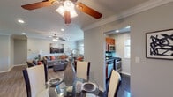 This single-floor residence at Fairfield at Hauppauge offers a thoughtfully designed layout that connects living, dining, kitchen, and sleeping areas in a cohesive, functional flow. Crown molding and ceiling fans are consistent throughout, lending a polished, uniform character to the interior.

The living room is comfortably proportioned, featuring wood-look flooring, recessed lighting, and a large window that invites natural light and outdoor views. The space transitions seamlessly into the dining area, which is distinguished by glossy dark tile flooring and a glass-top dining table with contrasting dark wood and white upholstered chairs.

The kitchen is a well-equipped galley-style space with rich cherry wood cabinetry, dark granite countertops, gleaming black tile floors, and stainless steel appliances including a gas range, built-in microwave, and refrigerator. A window above the sink provides additional natural light. An in-unit washer and dryer are also accommodated within the kitchen area.

The bedrooms are serene and generously sized, each featuring wood-look flooring, crown molding, ceiling fans, and ample closet storage. Natural light filters through windows with views of the surrounding greenery, contributing to a calm and restful atmosphere throughout.