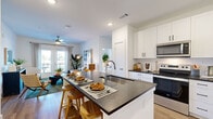 This single-floor residence is designed with a clean, contemporary aesthetic carried consistently throughout. The open-concept kitchen serves as a central hub, equipped with stainless steel appliances, white shaker cabinetry, dark granite countertops, and a spacious island with an undermount sink and bar seating — ideal for both meal preparation and casual dining. Light wood-style flooring flows seamlessly into the living area, where French doors invite natural light and provide access to an outdoor balcony. Ceiling fans are present in both the living room and bedrooms, contributing to comfort and airflow.

The primary bedroom is generously proportioned, featuring large windows with outdoor views, and connects directly to an en-suite bathroom outfitted with a dual-sink vanity, dark granite counters, white cabinetry, a glass-enclosed shower, and wood-look flooring. A spacious walk-in closet with wire shelving and carpeted flooring provides substantial storage. The second bedroom is equally well-appointed, with its own bathroom featuring a shower-tub combination. A flexible sitting nook near the living area offers additional functional space. Throughout, the white walls and recessed lighting create a bright, welcoming atmosphere.