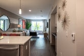 This contemporary single-floor residence showcases a thoughtfully designed open-concept layout that seamlessly connects the kitchen, dining, and living areas. Rich wood-look flooring flows throughout, complementing the clean, modern aesthetic.

The kitchen is a standout feature, equipped with stainless steel appliances including a refrigerator, range, and microwave. White gloss upper cabinetry is paired with warm wood-toned lower cabinets, while a mosaic tile backsplash adds texture and visual interest. A peninsula with a white quartz countertop and bar seating provides both additional workspace and a casual dining option. Pendant lighting above the peninsula enhances the kitchen's contemporary feel.

The open living area offers ample room for relaxation and entertaining, with natural light streaming in through large windows. The space features neutral gray walls accented with bold artwork, adding a modern, curated character to the room.

A louvered-door closet and additional storage solutions contribute to the unit's functional design. The bathroom features a bold red accent wall, a wood-toned vanity with an undermount sink, a large mirror, and a tub-shower combination, blending practicality with a striking visual style.

Overall, this residence delivers a cohesive modern design with quality finishes and a versatile, open floor plan.