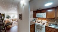 This single-floor residence offers a well-organized layout that connects its main living spaces in a practical and cohesive manner. The kitchen is outfitted with warm-toned wood cabinetry, granite-style countertops, a tiled backsplash in earthy hues, and white appliances including an electric range and over-the-range microwave. A stainless steel sink is positioned beneath upper cabinets, maximizing storage and counter workspace throughout the compact but functional area.

Adjacent to the kitchen, the dining area accommodates a round wooden table and chairs, accented by a pendant floor lamp and nature-inspired wall art, creating an intimate setting for meals. The living room is generously proportioned, featuring dark hardwood-style flooring, a textured ceiling, and a front-facing window that draws in natural light. Neutral-toned sofas, a glass-top coffee table, and greenery contribute to a calm, welcoming atmosphere.

The bedroom provides comfortable accommodations with a double-door closet, dark hardwood-style flooring, a window with soft drapery, and ample space for furniture. The bathroom includes a tub-shower combination with a decorative curtain, a vanity with cabinetry, and coordinated accents. Throughout the home, a consistent warm and inviting aesthetic ties each room together seamlessly.