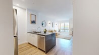 Located at 25 Maple Ave in New Rochelle, NY, this thoughtfully designed one-bedroom, one-bathroom residence offers a modern and efficient layout across a single floor. Light hardwood flooring flows throughout, complementing the clean white walls and contemporary finishes that define the space.

The open-concept kitchen and dining area serves as the heart of the home, featuring white cabinetry, stainless steel appliances including a refrigerator, microwave, and dishwasher, a classic subway tile backsplash, and a dark stone peninsula with bar seating — ideal for casual dining and entertaining. The adjacent living room is bright and welcoming, with large floor-to-ceiling windows that frame urban views of the New Rochelle skyline and fill the space with natural light.

The bedroom is generously proportioned, offering large windows with city views, two closets for ample storage, and a calm, airy atmosphere. The bathroom is finished with large-format marble-style tile on both the floors and walls, paired with a light wood vanity and a clean, minimalist aesthetic.

Additional conveniences include in-unit laundry and two dedicated closets. This well-appointed residence combines modern design with practical functionality in a vibrant New Rochelle location.