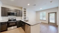 Located on Jupiter Road in Plano, TX, this single-story, one-bedroom, one-bathroom unit is thoughtfully designed to maximize functionality within a compact footprint. Light-toned hardwood-style flooring flows consistently throughout, creating a cohesive and clean aesthetic across all rooms.

The kitchen serves as a standout feature, equipped with stainless steel appliances including a refrigerator, electric range, built-in microwave, and dishwasher. Dark espresso cabinetry contrasts elegantly with the light granite countertops, which extend to a peninsula with an undermount sink. Open shelving adds additional storage and display space.

The bedroom is a comfortable, well-lit space featuring a ceiling fan, a large window with outdoor views, and neutral walls that create a bright, airy atmosphere. It connects to a dedicated walk-in closet outfitted with multi-level shelving and clothing rods along two walls, offering generous organization potential.

The bathroom features a full tub-shower combination with tiled surround, a dark-cabineted vanity with granite countertops, dual sinks, and a large mirror with vanity lighting. A hallway connects the main living areas, maintaining a practical and efficient layout throughout the unit.