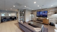 Located at 700–728 N Dearborn St in Chicago's vibrant River North neighborhood, this single-floor amenity space delivers a well-appointed environment designed for relaxation, entertainment, and community gathering. The lounge area anchors the space with a curved dark leather sofa, accent chairs, and a bold reclaimed wood feature wall hosting a large flat-screen TV, all illuminated by recessed lighting and complemented by open shelving with decorative accents. An adjacent seating nook features an eye-catching geometric gold pendant light, etched glass-paneled doors, and light tile flooring, providing a welcoming transition between areas. A separate lounge zone showcases a sculptural branching chandelier with globe bulbs, framed cityscape photography, and a gold-toned circular coffee table, creating an upscale yet inviting atmosphere. The fully equipped kitchen includes dark espresso cabinetry, black granite countertops, a white subway tile backsplash, and a full suite of stainless steel appliances. The game room stands out with high bar-height tables, counter seating along the windows, a foosball table, a shuffleboard table, and views of the Chicago skyline, making it a dynamic space for social engagement.
