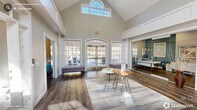 Located at 2105 Sheltonham Way in Raleigh, NC, this thoughtfully designed single-floor space offers a compelling blend of architectural grandeur and functional layout. The centerpiece is a dramatic living room boasting soaring vaulted ceilings, floor-to-ceiling arched French doors, and a striking clerestory window that floods the space with natural light. A monumental stacked-stone fireplace anchors the room, rising to the full height of the cathedral ceiling and creating a bold focal point. Rich hardwood flooring runs throughout, lending warmth and continuity across all areas. The dining room features elegant wainscoting, crown molding, and large multi-pane windows that bring in abundant daylight, complemented by a decorative mirrored sideboard. The dedicated office is a versatile, well-lit workspace outfitted with built-in desk surfaces, comfortable seating areas with accent chairs, and curated artwork, making it equally suited for collaborative work or quiet focus. Two connecting hallways guide the flow between spaces, with one hallway revealing teal accent walls and built-in package lockers. The overall ambiance is polished and professional, combining classic architectural details with contemporary furnishings for a refined, welcoming environment.