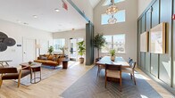 Located at 235 McDonough Rd in McDonough, Georgia, this single-floor community lounge is a thoughtfully designed gathering space that blends modern aesthetics with welcoming comfort. The open-concept layout is anchored by dramatic vaulted ceilings that rise to a striking peak, allowing generous natural light to pour in through large windows and clerestory glazing, offering views of the surrounding exterior. The space is divided into distinct yet connected zones. A lounge area features warm wood-look flooring and serves as a comfortable retreat with ample seating and tasteful décor, including lush potted greenery that adds life and vibrancy. Adjacent to it, a dining zone is defined by charcoal herringbone-pattern tile flooring and centers around a large communal table set beneath a sculptural geometric pendant light. This area is framed by a bold sage-green board-and-batten accent wall adorned with framed artwork. A kitchenette along one wall showcases slate-blue cabinetry, stainless steel appliances, a white countertop, and a patterned geometric wallcovering — a functional yet visually dynamic feature. Teal structural columns punctuate the space, reinforcing the cohesive color palette. Additional private rooms are accessible through the lounge, offering flexibility for various uses. The overall ambiance is bright, modern, and inviting.