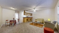 This single-floor residence in McAllen, Texas, offers a functional and cohesive layout designed for comfortable everyday living. The open-concept main living area serves as the heart of the home, featuring plush carpeting, a textured ceiling, and a ceiling fan that promotes airflow throughout the space. A built-in bar-top peninsula with warm wood cabinetry and glass-front upper cabinets separates the living area from the kitchen zone, providing seating for casual dining or entertaining.

The full kitchen is appointed with light wood cabinetry, glass-front upper cabinets, white appliances including a range, refrigerator, and dishwasher, all set atop warm hardwood flooring. Ample counter space and under-cabinet storage make this kitchen highly practical.

Adjacent to the main living space, a dining area accommodates a table and chairs, with natural light filtering in through a nearby window. The bedroom is a quiet, carpeted retreat with neutral-toned walls and a ceiling fan overhead, offering a calm and restful environment.

The bathroom features light wood cabinetry, a wide vanity with generous counter space, a mirror, and a shower-tub combination, all finished with hardwood flooring for easy maintenance. Overall, this residence presents a well-organized and inviting layout in a convenient McAllen location.