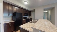 Located at 950 Brushfield Dr in Galloway, Ohio, this single-floor residence offers a well-designed layout with a cohesive, modern aesthetic throughout. The kitchen serves as a central highlight, featuring rich dark espresso cabinetry that extends floor to ceiling, light granite-style countertops, a large breakfast bar island with seating overhang, and black appliances including a refrigerator, range, and built-in microwave. Light wood-style flooring in the kitchen adds warmth and contrast to the darker cabinetry. The open configuration of the kitchen connects seamlessly to the adjoining living areas, creating an inviting flow. The bedrooms are finished with plush wall-to-wall carpeting and warm neutral wall tones, with natural light entering through blinded windows. At least one bedroom features double closet doors providing generous storage capacity. The bathrooms maintain a consistent design language, each appointed with dark espresso vanity cabinetry, light granite-style countertops, a single basin sink, large mirrors, and chrome fixtures. One bathroom includes a shower stall with built-in shelving, while tile flooring adds a clean, practical finish. The textured ceilings and neutral color palette throughout lend the space a calm, unified atmosphere well-suited for everyday living.