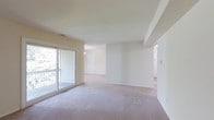 This single-floor residence offers a clean, open layout designed for comfortable everyday living. The main living area is generously proportioned, featuring wall-to-wall plush carpeting in a warm neutral tone that adds a sense of softness and ease underfoot. Smooth, light-colored walls throughout create a bright and airy atmosphere, complemented by natural light streaming in through a large sliding glass door that opens to a private balcony — an ideal spot to enjoy outdoor views and fresh air.

The open flow of the space connects the living area seamlessly to adjoining rooms, allowing for flexible furniture arrangements and a sense of continuity. Subtle architectural detailing, including a tray ceiling element in the living area, adds a layer of visual interest without disrupting the overall simplicity of the design. Additional doorways lead to further areas of the residence, suggesting a practical and well-organized floor plan. The neutral palette of whites and soft beiges throughout provides a versatile backdrop, making the space easy to personalize. Overall, the residence presents a tidy, move-in ready environment with a calm and inviting ambiance suited to a variety of lifestyles.