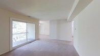 This single-floor residence offers a clean, open layout designed for comfortable everyday living. The main living area is generously proportioned, featuring wall-to-wall plush carpeting in a warm neutral tone that adds a sense of softness and ease underfoot. Smooth, light-colored walls throughout create a bright and airy atmosphere, complemented by natural light streaming in through a large sliding glass door that opens to a private balcony — an ideal spot to enjoy outdoor views and fresh air.

The open flow of the space connects the living area seamlessly to adjoining rooms, allowing for flexible furniture arrangements and a sense of continuity. Subtle architectural detailing, including a tray ceiling element in the living area, adds a layer of visual interest without disrupting the overall simplicity of the design. Additional doorways lead to further areas of the residence, suggesting a practical and well-organized floor plan. The neutral palette of whites and soft beiges throughout provides a versatile backdrop, making the space easy to personalize. Overall, the residence presents a tidy, move-in ready environment with a calm and inviting ambiance suited to a variety of lifestyles.