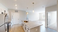 Located at 1745 Sledge Dr in Hilliard, Ohio, this well-appointed 2-bedroom, 2-bathroom single-story home offers a thoughtfully designed layout with modern finishes throughout. The open-concept kitchen and living area serves as the heart of the home, centered around a large granite-topped island with an undermount sink and stylish pendant lighting. White shaker-style cabinetry with matte black hardware, granite countertops, a tile backsplash, and stainless steel appliances — including a refrigerator, range, and over-the-range microwave — complete the kitchen. Light wood-look flooring flows seamlessly through the main living areas, complementing the neutral gray and warm beige wall tones. The living room benefits from natural light streaming through a large window. Both bedrooms are carpeted and generously sized, with the primary bedroom offering a comfortable retreat. The primary bathroom features a granite vanity with white cabinetry and access to a walk-in closet, while the second bathroom includes a walk-in shower. Two closets and a hallway provide practical storage. The home's clean, contemporary aesthetic and efficient single-floor layout make it an ideal residence in Hilliard.