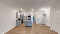 Located at 919 Woody Dr in Graham, NC, this single-floor unit presents a clean, contemporary design with thoughtful finishes throughout. The open-concept kitchen serves as the centerpiece of the living area, featuring gray shaker-style cabinetry, granite countertops, stainless steel appliances including a range with a stainless wall-mounted hood vent, built-in microwave, and refrigerator. A central kitchen island provides additional workspace and casual seating potential. Wood-look luxury vinyl plank flooring runs throughout the main living and kitchen areas, adding warmth and durability.

The bedrooms are carpeted for comfort and include ceiling fans with integrated lighting. Paired windows fitted with white blinds allow natural light to filter in while maintaining privacy. A spacious walk-in closet features wire shelving and hanging rods, offering generous storage capacity.

The bathrooms are well-appointed; one includes a walk-in glass-door shower, granite-topped vanity with gray cabinetry, and wood-look flooring, while another features a full tub-shower combination with tiled surround and built-in corner shelving. Additional storage is available via a dedicated pantry closet with wire shelving. The overall aesthetic is modern and move-in ready.