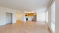 This modern single-floor unit offers a thoughtfully designed open-concept layout, seamlessly connecting the living area and kitchen into one expansive, light-filled space. Light hardwood-style flooring extends throughout the main living areas, complementing the clean white walls and creating a bright, airy ambiance. Large windows along the exterior walls invite generous natural light and offer views of the surrounding neighborhood.

The kitchen is efficiently designed in an L-shaped configuration, featuring warm wood-toned upper cabinetry paired with crisp white lower cabinets. A full suite of stainless steel appliances — including a refrigerator, range, dishwasher, and over-the-range microwave — provides modern functionality. Recessed lighting illuminates the workspace, and a sleek sink with contemporary fixtures completes the area.

The bedrooms are carpeted for comfort and each benefit from multiple windows fitted with horizontal blinds, offering both natural light and privacy. Sliding closet doors with built-in hanging rods provide practical storage solutions. A wall-mounted HVAC unit is present in the bedrooms for individualized climate control.

The bathrooms feature white cabinetry with satin-nickel hardware, a white quartz countertop, an undermount sink, and a backlit vanity mirror. Hardwood-style flooring and grab bars highlight both style and accessibility throughout the space.