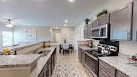 Located at 3151 Boulevard De Sevilla Blvd in Foley, Alabama, this single-story residence offers a thoughtfully designed open-concept floor plan with modern finishes throughout. The welcoming entryway features light wood-style flooring, a ceiling fan, and a window that fills the space with natural light. The living area flows seamlessly into the dining space, creating an ideal setting for everyday living and entertaining, with neutral tones and ceiling fans adding comfort throughout. The galley-style kitchen is a standout feature, showcasing granite countertops, dark taupe cabinetry, stainless steel appliances including a range, microwave, and refrigerator, and generous counter space on both sides. The kitchen opens directly to the dedicated dining area, which provides an intimate space for meals. The bedrooms offer plush carpeting, ceiling fans, natural light from windows, and walk-in closet storage. The bathrooms are finished with granite-topped vanities, dark cabinetry, brushed nickel fixtures, large mirrors, and well-lit vanity lighting. One bathroom includes a shower/tub combination. The consistent use of light wood-style flooring in the main living areas, neutral wall tones, and quality finishes throughout give the home a cohesive, contemporary feel.