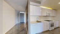This contemporary single-floor unit offers a thoughtfully designed layout encompassing one bedroom, two bathrooms, and a connecting hallway, totaling approximately 1,000 square feet of living space. Polished concrete floors run throughout, lending an industrial-chic aesthetic that is both durable and visually striking.

The open living area is defined by clean white walls and a dramatic floor-to-ceiling window that floods the space with natural light while offering views of the surrounding cityscape. A structural concrete column serves as an architectural accent, reinforcing the modern industrial character of the unit.

The kitchen features sleek, flat-front white cabinetry extending to the ceiling, a light-colored countertop, stainless steel sink, gas cooktop, and a dishwasher — all arranged for efficient use of space.

Built-in shelving and cabinetry in the hallway area provide generous storage solutions, complementing the minimalist design language found throughout.

The generously sized primary bedroom offers a calm, neutral palette with access to the adjoining spaces. Both bathrooms are finished in crisp white, with one featuring a soaking tub framed by classic subway tile, and the other serving as a clean, functional half bath — each with modern white vanities and polished fixtures that align with the overall contemporary aesthetic.