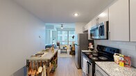 Located at 410 W Fayette St in the heart of downtown Baltimore, this thoughtfully designed studio offers a functional and modern single-floor layout. The open-concept living area seamlessly blends the kitchen, living, and sleeping zones into one cohesive space. Light wood-tone flooring runs throughout, contributing to a clean, contemporary aesthetic.

The kitchen is well-appointed with stainless steel appliances, including an electric range, over-the-range microwave, refrigerator, and dishwasher. Granite-style countertops, a subway tile backsplash, and sleek gray cabinetry provide both style and ample storage. A large window at the far end of the living and sleeping area floods the space with natural light and offers views of the surrounding urban cityscape. A ceiling fan adds practical comfort to the main living zone.

The bathroom features a granite-topped vanity with modern cabinetry, a backlit mirror, and light tile flooring, creating a crisp and bright atmosphere. A stacked washer and dryer unit is conveniently tucked within the bathroom area, providing in-unit laundry. The sleeping area accommodates a full-sized bed with closet access nearby. This unit delivers efficient urban living in a central Baltimore location.
