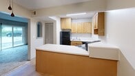 Located at 217 W Broadway in Columbia, Missouri, this single-floor unit offers three bedrooms, one bathroom, and a well-organized layout that makes efficient use of its space. The living area features soft carpeting and a sliding glass door that brings in natural light and provides outdoor access. A distinctive arched pass-through window connects the living space to the adjacent dining or secondary area, which features hardwood-style flooring and a ceiling fan overhead. The kitchen is equipped with light wood cabinetry, a tile backsplash, black appliances including a refrigerator, electric range, and dishwasher, and an extended peninsula countertop that offers additional prep and serving space. The three carpeted bedrooms feature neutral wall tones; the primary bedroom includes a double-door closet with direct access to the shared bathroom. The secondary bedrooms each have windows with blinds that allow natural light. The full bathroom features tile flooring, a tub-shower combination, and a vanity with wood cabinetry. A hallway connects the bedrooms to the main living areas, providing a cohesive and navigable floor plan throughout.