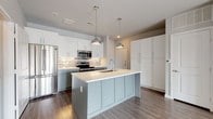 This single-floor residence offers a well-designed layout across two bedrooms and two full bathrooms. The kitchen serves as a central highlight, featuring a large center island with a light-colored quartz countertop, an undermount sink, and pendant lighting overhead. Two-toned cabinetry pairs soft sage lower cabinets with crisp white uppers, complemented by a mixed mosaic tile backsplash and a full suite of stainless steel appliances, including a French door refrigerator, electric range, and built-in microwave. Dark hardwood-style flooring grounds the kitchen and extends into adjacent areas, while a dedicated in-unit laundry space is conveniently accessible nearby.

The bedrooms feature plush neutral carpeting and soft gray walls. One bedroom includes French doors that invite natural light and provide outdoor access, while the other offers a clean, versatile layout. Both bathrooms are finished with light tile flooring, white cabinetry, and granite-style countertops. The primary bathroom includes a double-sink vanity with a large mirror, a walk-in glass shower with white tile surround, and a walk-in closet. The secondary bathroom features a tub-shower combination. Throughout, the space maintains a cohesive, modern aesthetic with clean lines and neutral tones.