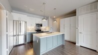 This single-floor residence offers a well-designed layout across two bedrooms and two full bathrooms. The kitchen serves as a central highlight, featuring a large center island with a light-colored quartz countertop, an undermount sink, and pendant lighting overhead. Two-toned cabinetry pairs soft sage lower cabinets with crisp white uppers, complemented by a mixed mosaic tile backsplash and a full suite of stainless steel appliances, including a French door refrigerator, electric range, and built-in microwave. Dark hardwood-style flooring grounds the kitchen and extends into adjacent areas, while a dedicated in-unit laundry space is conveniently accessible nearby.

The bedrooms feature plush neutral carpeting and soft gray walls. One bedroom includes French doors that invite natural light and provide outdoor access, while the other offers a clean, versatile layout. Both bathrooms are finished with light tile flooring, white cabinetry, and granite-style countertops. The primary bathroom includes a double-sink vanity with a large mirror, a walk-in glass shower with white tile surround, and a walk-in closet. The secondary bathroom features a tub-shower combination. Throughout, the space maintains a cohesive, modern aesthetic with clean lines and neutral tones.