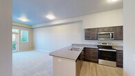 Located at 13525 E Carlisle Ave in Spokane Valley, WA, this two-bedroom, two-bathroom residence offers a well-organized single-floor layout designed for comfortable everyday living. The open-concept kitchen and living area serves as the heart of the home, featuring stainless steel appliances—including a refrigerator, electric range, and microwave—dark cabinetry with brushed nickel hardware, and a generous countertop with a double-basin sink that overlooks the carpeted living space. The living room receives abundant natural light through a glass door and flanking windows that lead to a private balcony with views of the surrounding community. Both bedrooms are carpeted and well-proportioned, with the primary bedroom offering a dedicated closet and direct access to its own bathroom. The bathrooms are finished with light wood-look flooring, dark vanity cabinetry, white countertops, and chrome fixtures; one features a tub-shower combination while the other includes an accessible shower with a grab bar. A dedicated closet provides additional storage. Neutral warm tones, clean white trim, and consistent finishes throughout lend the space a cohesive, move-in-ready appeal.