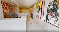 This 260 square foot facility in Irvine, California is a thoughtfully designed pet grooming space. The single-floor layout maximizes functionality in a compact area. Upon entry, glass doors flood the space with natural light, offering views of the surrounding greenery. The interior boasts a clean, modern aesthetic with cream-colored walls and floors, accented by vibrant red and orange tiled sections that add warmth and energy to the environment. A standout feature is the professional-grade stainless steel grooming station, complete with steps for easy pet access. The space is further enhanced by playful, oversized portraits of dogs, adding a touch of whimsy to the professional setting. Practical elements include recessed lighting, a circular mirror, and a sleek counter area. This well-equipped facility combines functionality with a welcoming atmosphere, catering to both the practical needs of pet grooming and the comfort of its furry clients.