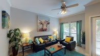 This single-story, 2-bedroom, 2-bathroom residence offers a functional and cohesive layout designed for comfortable everyday living. The living room serves as the central gathering space, featuring tile flooring, a ceiling fan with light fixture, and a large window dressed with teal curtains that invite natural light. Crown molding adds a refined architectural touch to the room.

The kitchen is equipped with stainless steel appliances, including a range, microwave, and refrigerator, complemented by granite-style countertops, light wood cabinetry, and tile flooring. A breakfast bar with bar seating connects the kitchen to the adjacent hallway, creating an open, accessible flow between spaces.

The primary bedroom is generously proportioned, featuring plush carpeting, a ceiling fan, and a window that brings in natural light. The second bedroom is similarly carpeted and well-sized, offering comfortable accommodations. Both bathrooms include vanities with ample cabinet storage and tile flooring, with at least one bathroom featuring a walk-in shower.

A dedicated in-unit laundry room houses a full-sized washer and dryer alongside built-in shelving for added storage convenience, completing this practical and well-designed residence.