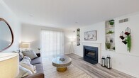 This single-floor residence offers a thoughtfully designed layout that balances comfort and modern style throughout. The living room serves as the heart of the home, showcasing light hardwood-style flooring, crisp white walls, and crown molding that adds a refined architectural touch. A classic fireplace with a white surround anchors the space, flanked by built-in shelving units that provide both storage and display opportunities. A large sliding glass door fitted with vertical blinds allows natural light to fill the room while offering access to the outdoors.

The galley-style kitchen is efficiently arranged with ample white cabinetry, dark granite countertops, and stainless steel appliances, including a refrigerator and range. The clean, bright layout maximizes functionality without sacrificing style.

The bedroom is a calm retreat, featuring light-filled windows dressed with sheer curtains and wood blinds, continuing the same hardwood-style flooring found throughout the home. The bathroom is clean and well-appointed, featuring a full soaking tub and shower combination with white surround, wood-toned flooring, and a vanity with dark stone countertops that echo the kitchen's design. The overall ambiance of the space is light, airy, and cohesive, with a neutral palette that feels both welcoming and contemporary.
