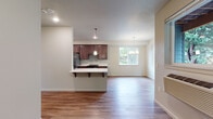 Located at 8527 NE Quatama St in Hillsboro, Oregon, this single-floor unit offers a well-organized layout designed for functional everyday living. The open-concept kitchen and living area serves as the heart of the space, where warm wood-look flooring flows throughout. The kitchen is outfitted with rich dark cabinetry, white countertops, a subway tile backsplash, and stainless steel appliances including a refrigerator, range, and dishwasher. A peninsula with bar seating provides additional prep and dining space, while pendant lighting adds a polished touch above. Adjacent to the kitchen, the dining and living area benefits from natural light through a large window, with a chandelier-style fixture overhead enhancing the ambiance.

A hallway connects to the bedroom, which features plush carpet flooring and two generously sized windows that bring in ample natural light and neighborhood views. A louvered closet door provides organized storage nearby. The bathroom includes a full tub and shower combination with a handheld showerhead, a toilet, and open built-in shelving that offers convenient storage. Neutral wall tones and consistent finishes throughout give the space a clean, cohesive feel.