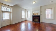 Located at 4601 Spruce St in Philadelphia's West Philadelphia neighborhood, this single-floor residence blends classic architectural charm with functional living spaces. The living room immediately draws attention with its stunning herringbone-pattern parquet hardwood floors, which gleam with a rich, deep mahogany tone. A decorative fireplace with a dark wood mantel and mosaic tile surround serves as the room's focal point, while multiple windows along the walls allow natural light to fill the space. Crown molding and clean white walls contribute to a refined, traditional aesthetic. An open pass-through connects the living area to the kitchen, offering a sense of connectivity between the two spaces. The kitchen is well-equipped with warm oak cabinetry, a gas range, dishwasher, and refrigerator, all complemented by white tile backsplash and tile flooring. A window above the kitchen area brings in additional natural light. The bedrooms feature plush blue carpeting and are bright with multiple large windows providing ample daylight. Built-in closets and panel-style doors add classic detail throughout. The bathroom is finished with light tile flooring, full wall tiling, a vanity with wood cabinetry, and a window for natural ventilation. Overall, the space offers a well-preserved, characterful interior with timeless design elements.