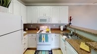 This single-floor 2-bedroom, 1-bathroom residence offers a thoughtfully designed layout with a neutral gray color palette and clean white trim throughout. The open living area is bright and welcoming, featuring plush carpeting, crown molding, and a ceiling fan. A sliding glass door floods the space with natural light and provides access to an outdoor area. The kitchen is well-equipped with white cabinetry, granite-style countertops, white appliances including a range, microwave, and refrigerator, and durable tile flooring. A granite-topped breakfast bar extends from the kitchen into the dining area, offering a casual dining or workspace option. Both bedrooms are generously sized with soft carpeting, neutral gray walls, and windows fitted with blinds that allow for natural light. The primary bedroom includes two closets — one standard and one walk-in — providing ample storage. The full bathroom is finished with tile flooring, white cabinetry, granite-style countertops, a large vanity mirror with overhead lighting, and a full tub-shower combination. The overall design is clean, functional, and move-in ready, with consistent finishes that create a cohesive and comfortable living environment.