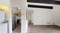 This 600-square-foot, one-bedroom, one-bathroom apartment at 300 Buckminster Dr in Norwood, MA offers an efficiently designed single-floor layout. The living room is an immediate standout, featuring soaring vaulted ceilings adorned with bold, dark exposed wooden beams that add architectural character. Large sliding glass doors flood the space with natural light and open directly onto a private balcony overlooking well-maintained community grounds, lush green lawns, and mature trees. The hardwood-style luxury vinyl flooring runs consistently throughout the unit, creating a cohesive, modern aesthetic. The kitchen is equipped with stainless steel appliances including a full-size refrigerator, dishwasher, and built-in microwave, complemented by warm-toned wood cabinetry and light marble-style countertops. The spacious primary bedroom spans 210 square feet and mirrors the living area's vaulted ceiling with exposed beams, along with a large window offering natural light and outdoor views. The bathroom features a clean, neutral design with white cabinetry, a round mirror, wood-tone vinyl flooring, and brushed gold accent hardware, providing a polished and functional finish throughout.