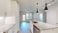 This thoughtfully designed single-floor residence combines contemporary finishes with a functional, open layout. The kitchen serves as the centerpiece, outfitted with crisp white shaker cabinetry, light granite countertops, a full suite of stainless steel appliances including a refrigerator, range, microwave, and dishwasher, and a large island with an undermount sink. Stylish pendant lighting accents the island, while under-cabinet lighting illuminates the tile backsplash and ample counter space below.

The kitchen flows seamlessly into the living area, which is bathed in natural light from multiple windows fitted with horizontal blinds. Light-toned luxury vinyl plank flooring extends throughout the space, lending a clean, cohesive feel. A ceiling fan keeps the living area comfortable, and a private exterior door provides convenient access.

The primary bathroom is well-appointed with a granite-topped vanity, grey cabinetry, a soaking tub with tiled surround, and wood-look flooring. An adjacent walk-in closet offers generous built-in shelving and hanging rods, providing excellent organization and storage capacity.

A separate bedroom features a ceiling fan, dual windows with outdoor views, and the same light flooring found throughout, creating a bright and airy retreat. The overall aesthetic is modern, clean, and move-in ready.