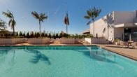 Located at 18750 Delaware St in Huntington Beach, California, this expansive outdoor amenity deck offers a resort-style experience in the heart of Southern California's coastal community. The centerpiece of the space is a generously sized swimming pool with crystal-clear turquoise water, complemented by a separate spa and whirlpool area ideal for relaxation. The pool deck is finished in warm, light-toned pavers that reflect the abundant natural sunlight characteristic of the region.

Surrounding the pool, a thoughtfully arranged collection of lounge chairs and chaise lounges provides ample space for sunbathing and leisure. Private cabanas with louvered shading structures offer more intimate retreats, furnished with comfortable seating for small groups. A covered bar or lounge structure serves as a central gathering point on the deck.

Tall, swaying palm trees punctuate the space, lending a distinctly tropical ambiance, while raised planter beds filled with lush greenery and manicured shrubs define the perimeter and add natural texture. The open layout allows for panoramic views of the surrounding skyline and blue skies above.

The overall design blends clean, modern architecture with resort-inspired outdoor living, creating a welcoming and upscale environment perfectly suited to the warm Huntington Beach climate.