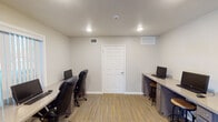 This single-story community office, located along S Gessner Rd in Houston, TX, is designed to serve as a welcoming and functional hub. The entrance features glass double doors that allow natural light to pour into the space, complemented by wood-look tile flooring and neutral-toned walls that carry throughout the interior.

The main area offers an open and airy layout, anchored by a warm-toned wooden reception desk accompanied by guest seating. Recessed lighting illuminates the space evenly, while a wall-mounted flat-screen television and a dedicated seating lounge near the front windows create a comfortable, approachable environment for visitors.

A built-in workstation area is integrated along one wall, featuring granite-topped counters with desktop computers and bar-height stools, providing convenient self-service access points. A separate, enclosed business center room offers additional computer workstations with built-in desks on both sides of the room, ergonomic seating, and its own HVAC venting, making it suitable for focused tasks in a quieter setting. The room is finished with striped vinyl plank flooring and recessed ceiling lighting. Overall, the space balances a professional aesthetic with practical amenities in a clean, well-maintained setting.