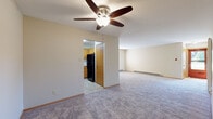 Located at Waterford Square in Greenfield, Wisconsin, this single-floor unit offers a practical and comfortable layout designed for everyday living. The open living area is anchored by a ceiling fan with light fixture and features wall-to-wall carpeting, baseboard heating, and neutral-toned walls that create a clean, bright atmosphere. A sliding glass door with vertical blinds leads to the entry, allowing natural light to filter into the space. The kitchen is efficiently arranged with warm oak cabinetry, white countertops, and a suite of black appliances including an electric range, over-the-range microwave, and refrigerator. Tile flooring in the kitchen provides a practical transition from the carpeted living areas. The bedroom is generously proportioned, finished with plush carpet, a large window overlooking mature trees, and baseboard heating. The full bathroom features oak vanity cabinetry with a white countertop, tile flooring, and a dedicated tub and shower combination with a clean white surround. Throughout the unit, consistent wood trim accents and neutral wall colors contribute to a cohesive, move-in-ready feel. The layout is straightforward and functional, making efficient use of the available space across its single floor.