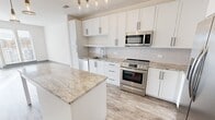 Located at 1925 Roland Clarke Place in Reston, Virginia, this thoughtfully designed one-bedroom residence offers a clean, contemporary aesthetic throughout its single-floor layout. The open-concept kitchen serves as a focal point of the home, showcasing crisp white shaker cabinetry with matte black hardware, granite countertops with elegant veining, and a full suite of stainless steel appliances including a range, built-in microwave, refrigerator, and dishwasher. A central island with a matching granite surface provides additional prep space and casual seating, while stylish pendant lighting adds a warm, modern touch overhead. Wood-look luxury vinyl flooring runs through the main living areas, complementing the light-filled, neutral color palette. The living area features large glass doors that invite generous natural light and offer views of the surrounding outdoor scenery. The bedroom is carpeted for comfort, with a bright window and a panel-style door that adds architectural detail. A dedicated walk-in closet includes multi-level wire shelving and hanging rods, offering well-organized storage. Throughout the space, clean white walls, gray base trim, and modern finishes create a cohesive and inviting atmosphere ideal for contemporary living in the heart of Reston.