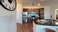 This single-story residence is thoughtfully designed with a cohesive aesthetic and functional layout. The living room is a standout space, featuring an abundance of natural light streaming through a bank of large windows fitted with blinds, dark hardwood-style flooring, crown molding, and a wall-mounted flat-screen television. A private entry door with a glass panel enhances connectivity to the outdoors.

Adjacent to the living area, the dining space accommodates a round table with seating for four, complemented by warm neutral walls and consistent flooring. The kitchen is well-equipped with rich dark wood cabinetry, stainless steel appliances including a refrigerator, electric range, and built-in microwave, granite-style dark countertops, a tile backsplash, and track lighting overhead.

The bedroom is a tranquil retreat with teal curtains framing windows that offer outdoor views, dark hardwood-style flooring, and ample space. A generously sized walk-in closet features wire shelving and hanging rods along multiple walls for organized storage. The bathroom includes a full tub-shower combination with white subway tile surround and classic fixtures, completing this well-rounded residence.