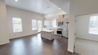 This single-floor residence is designed with a clean, contemporary aesthetic that emphasizes open living and functional layout. The heart of the home is an open-concept kitchen and living area, where light-toned flat-front cabinetry, a subway tile backsplash, and a full suite of stainless steel appliances — including a gas range, microwave, dishwasher, and refrigerator — create a well-equipped culinary space. A central island with a bright white countertop provides additional prep space and serves as a natural gathering point. Pendant lighting and recessed fixtures illuminate the area, while large windows allow natural light to fill the open living zone, which features rich, dark hardwood-style flooring throughout.

The bedrooms are carpeted and bright, each receiving natural light through windows fitted with horizontal blinds. One bedroom includes an ensuite bathroom equipped with a glass-enclosed walk-in shower and white tile surround, along with a dedicated closet. Additional bedrooms offer sliding-door closets. A second bathroom features a full soaking tub with a tiled surround and a curved shower rod. The overall palette is neutral and light, with white walls, clean lines, and modern hardware contributing to a cohesive, move-in-ready atmosphere.