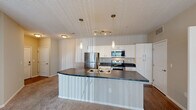 Located at 2000 Burgess Dr in Uniontown, Ohio, this single-floor, 2-bedroom, 2-bathroom home offers a well-designed layout with a thoughtful blend of comfort and functionality. The open-concept kitchen is a standout feature, showcasing white shaker cabinetry extending to the ceiling, dark countertops, and a full suite of stainless steel appliances including a refrigerator, electric range, and over-the-range microwave. A large peninsula island with a double sink provides additional workspace and separates the kitchen from the living area, which is finished with plush carpet and a sliding glass door that floods the space with natural light and provides outdoor access. The primary bedroom is generously proportioned and includes a walk-in closet with dual wire shelving. The second bedroom features carpet flooring, a bright window with outdoor views, and convenient access to in-unit laundry. Both bathrooms are finished with white vanity cabinetry, dark countertops, and well-lit mirrors. Hardwood-style flooring anchors the kitchen and entry areas, while neutral-toned carpet runs throughout the bedrooms and living spaces, creating a warm, cohesive ambiance throughout the home.