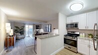 Located at 3801 Conshohocken Ave in Philadelphia's 19131 neighborhood, this well-appointed one-bedroom, two-bathroom residence offers a thoughtfully designed single-floor layout. The open-concept kitchen and living area serves as the heart of the home, where a granite-topped peninsula breakfast bar connects the two spaces seamlessly. The kitchen is outfitted with stainless steel appliances — including a gas range, over-the-range microwave, and refrigerator — complemented by crisp white shaker cabinetry and light hardwood-style flooring. The living room offers plush carpeting, neutral tones, and a sliding glass door that floods the space with natural light and provides direct access to an outdoor area. The spacious primary bedroom features soft carpeting, generous proportions, and a calm, neutral palette conducive to rest. Two bathrooms serve the unit: one features a clean white vanity with brushed nickel fixtures, while the second includes a full soaking tub and shower combination with white tile surround and hardwood-style flooring. A dedicated closet provides practical storage. Throughout the residence, a cohesive design language of warm neutrals, modern finishes, and functional layouts creates a comfortable and inviting atmosphere.