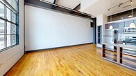 This urban loft in downtown Winston-Salem blends industrial character with modern finishes. The open living area features warm hardwood floors, exposed steel beams, and dramatic factory-style windows that flood the space with natural light and frame downtown city views. The kitchen is equipped with rich dark wood cabinetry, granite countertops, stainless steel appliances, and pendant lighting. The bedroom includes two generous closets with built-in shelving. Both bathrooms feature large-format tile flooring, tub-shower combos, and dark wood vanities with granite countertops, echoing the cohesive design throughout.