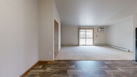 Located at 540 McKinley Ave in Clintonville, Wisconsin, this two-bedroom, one-bathroom unit offers a practical and comfortable single-floor layout. The open-concept kitchen and living room form the heart of the space, with wood-look plank flooring throughout the kitchen area transitioning to plush carpet in the living room. The kitchen is equipped with warm oak cabinetry, light countertops, and a full suite of black appliances including a refrigerator, dishwasher, gas range, and microwave. A sliding glass door in the living area opens to a private balcony, allowing natural light to fill the room. A wall-mounted A/C unit and baseboard heating provide year-round climate control. Both bedrooms feature soft carpeting, ceiling fans, and ample natural light from windows with views of the surrounding area. The primary bedroom includes access to a spacious walk-in closet with built-in shelving and hanging rods for generous storage. An additional bedroom features a bifold closet. The full bathroom offers a single-sink vanity with oak cabinetry, a tub-shower combo, and wood-look flooring consistent with the rest of the unit. A dedicated closet rounds out the storage options in this well-organized and move-in ready space.